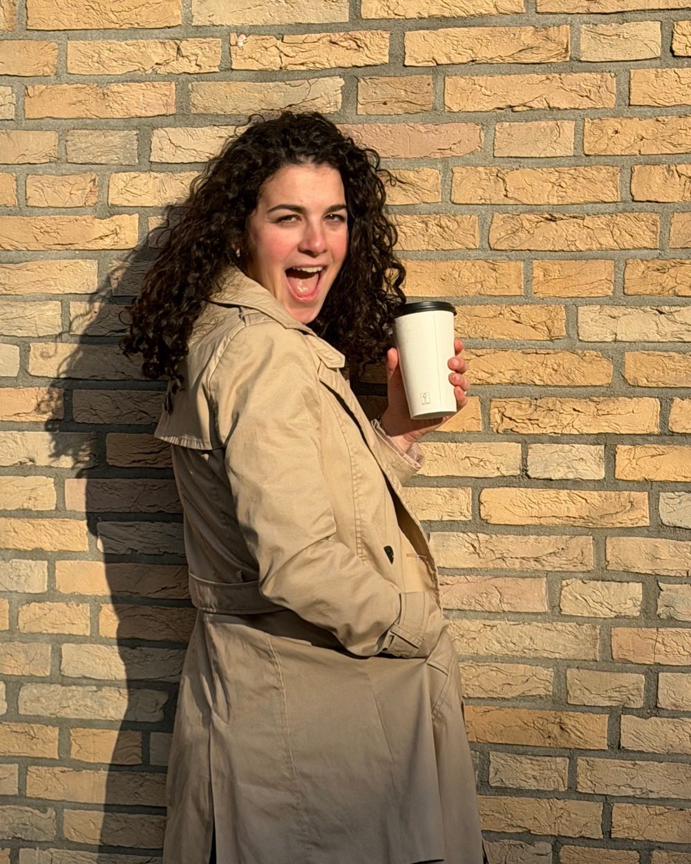 Julika mit Kaffee vor einer Backsteinwand